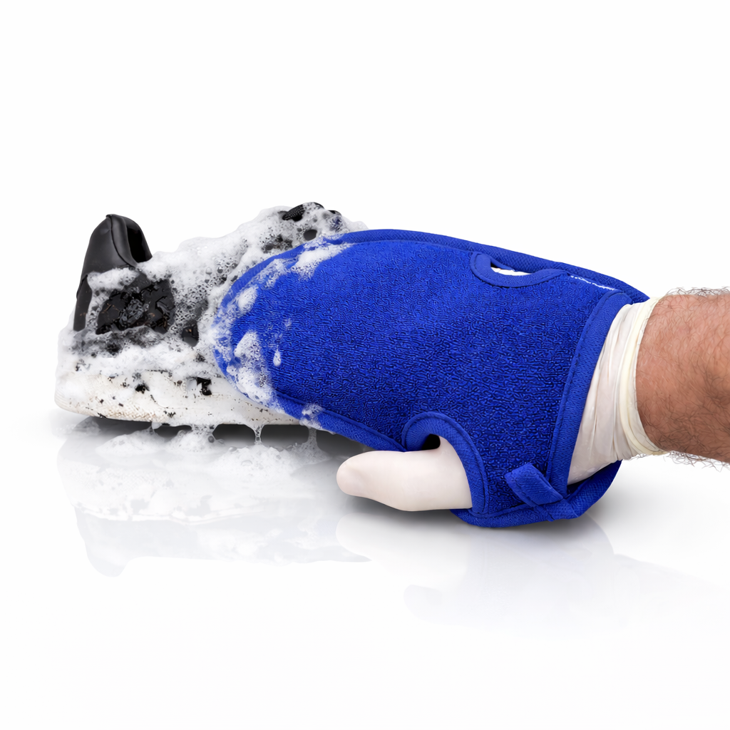 Hand wearing a blue mitt scrubbing a black shoe with soap on a white background