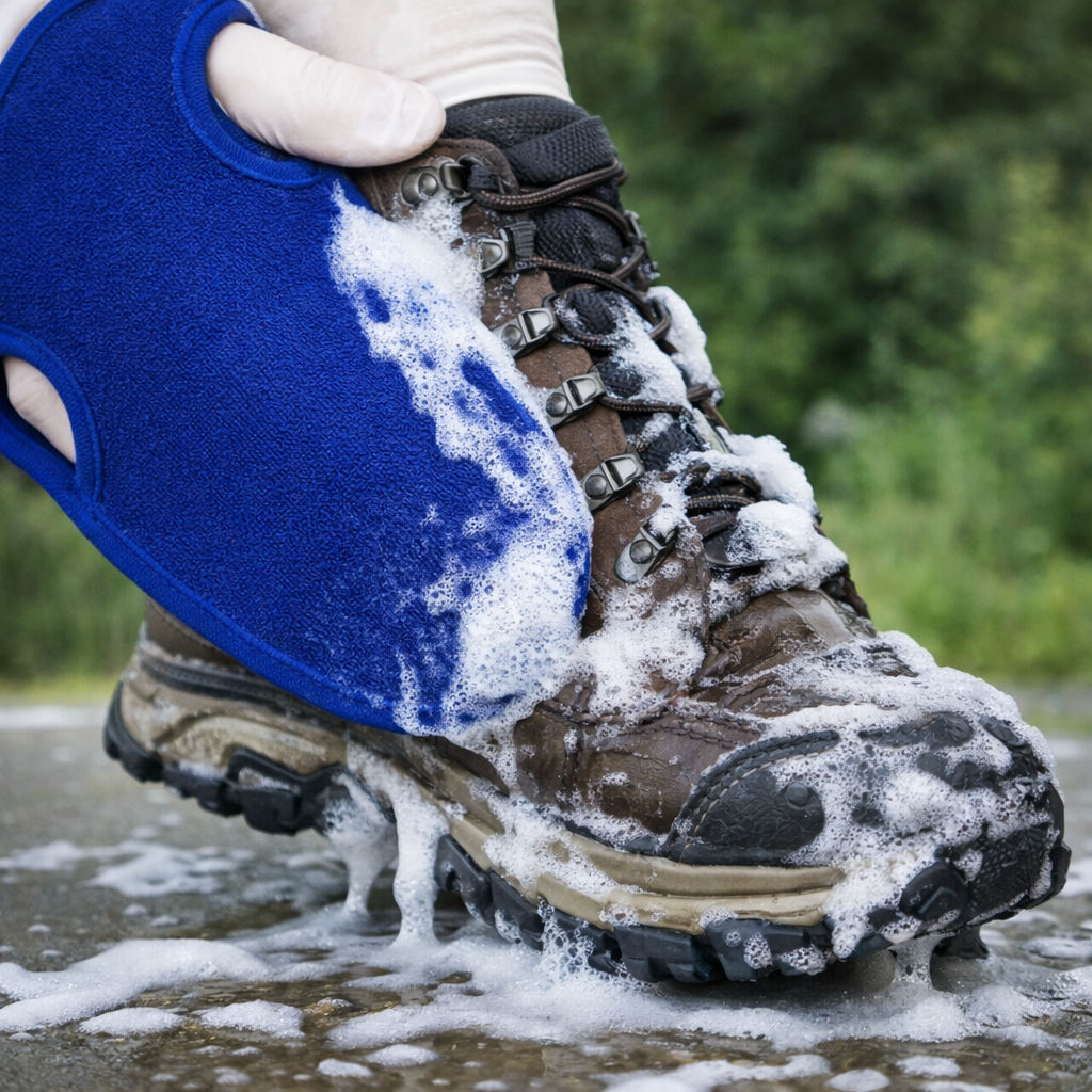 Person cleaning a brown hiking boot with a blue cleaning mitt outdoors.